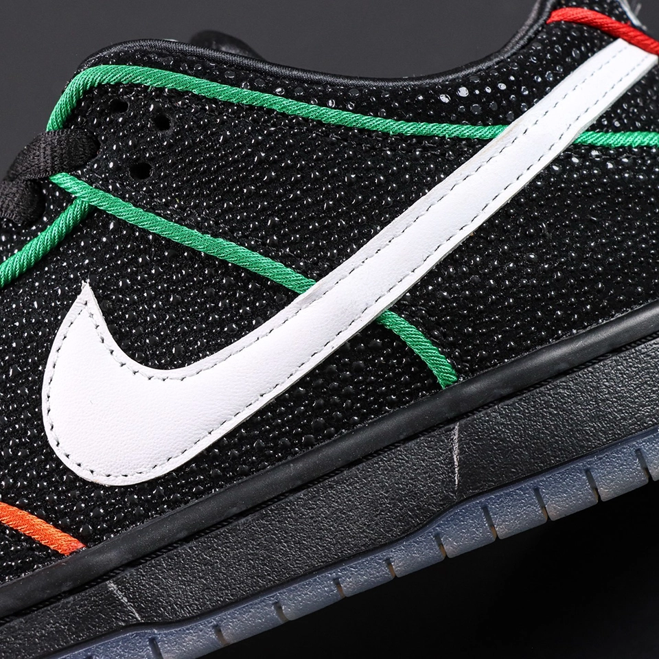 Detailed close-up of Bronx Girls Skate x Nike Dunk Low SB ‘Mel & Kava’ white leather Swoosh on black textured upper with green trim