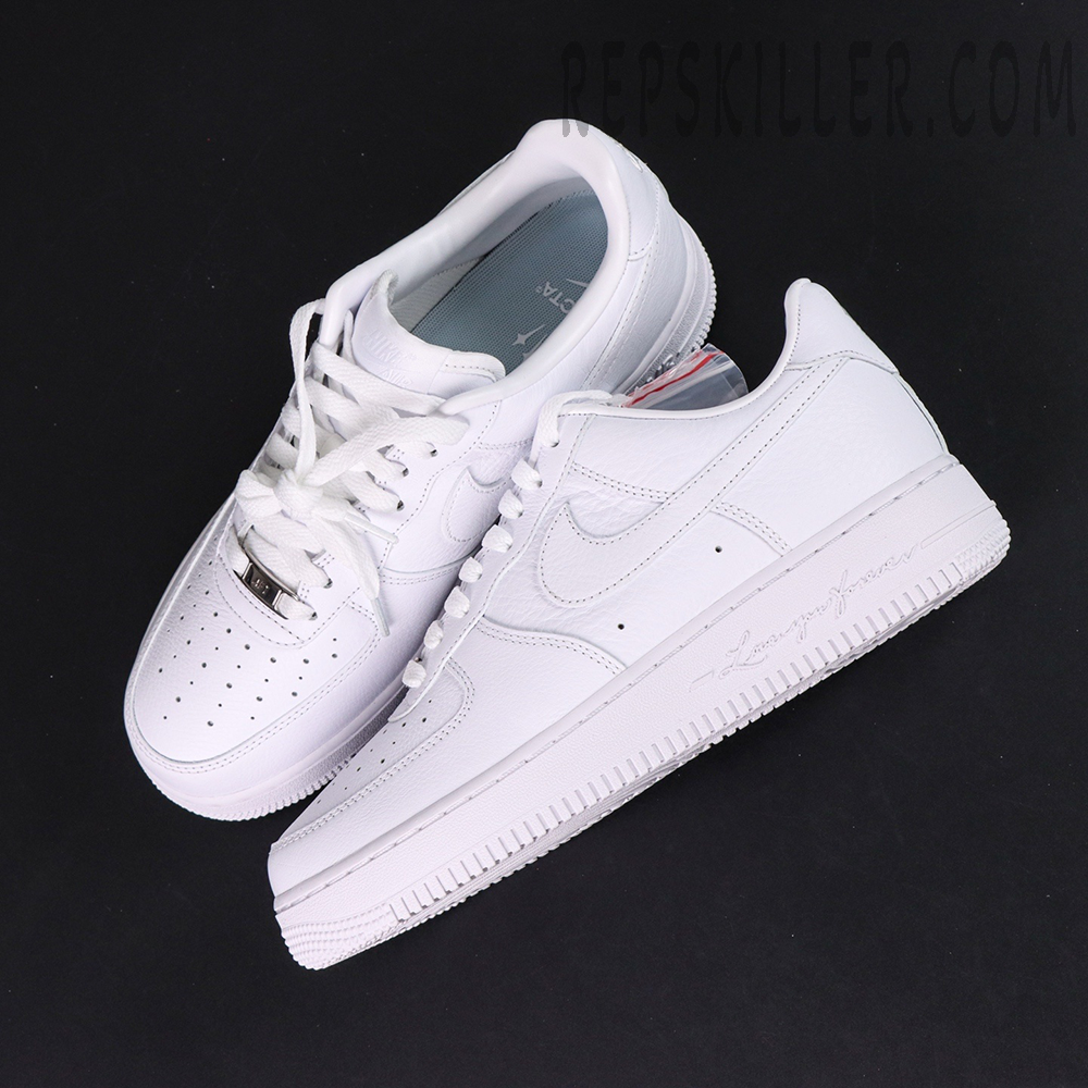 Overhead pair of NOCTA x Nike Air Force 1 Low “Certified Lover Boy” showing premium white tumbled leather and engraved midsole text.