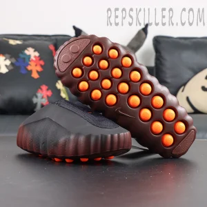 Nike Mind 001 Flyknit “Bronze Eclipse” outsole view featuring a dark brown sole with vibrant orange cushioning pods for striking contrast